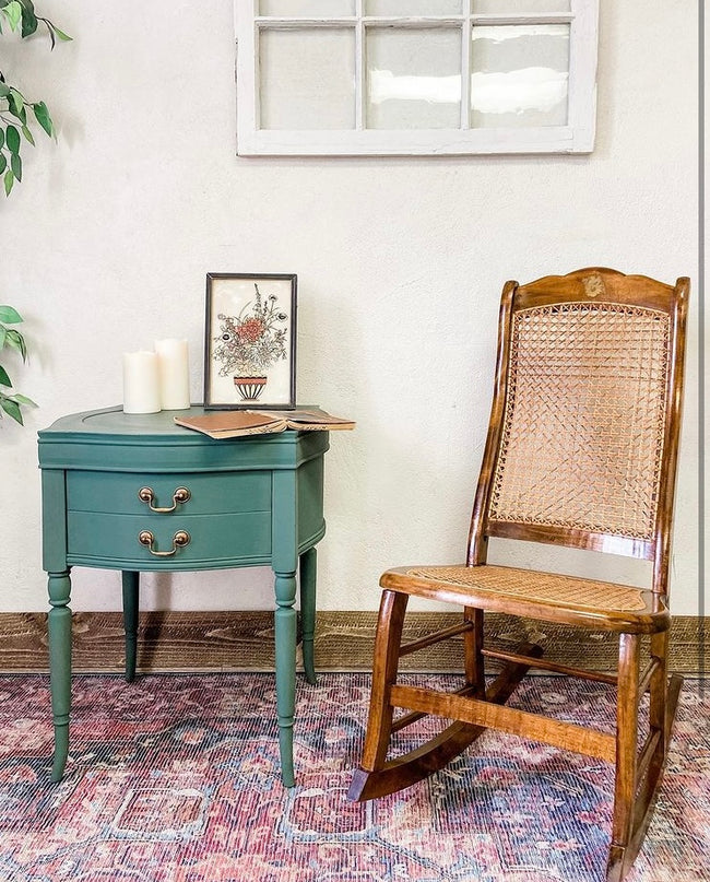 Dark green painted end table with old white window frame wall decor and wooden rocking chair