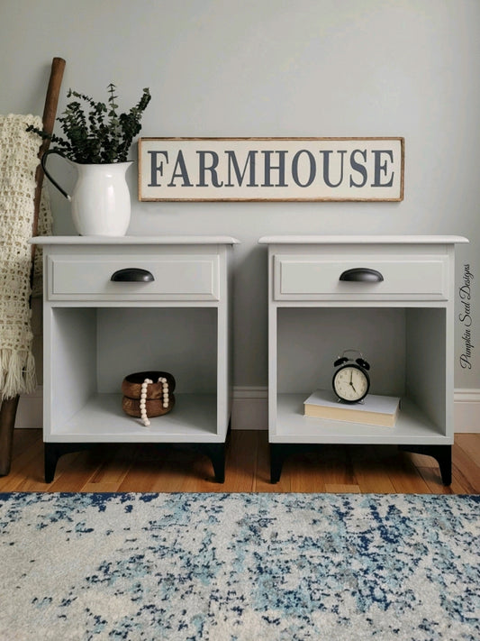 Light grey matching nightstands with black cup pulls black legs and a farmhouse sign