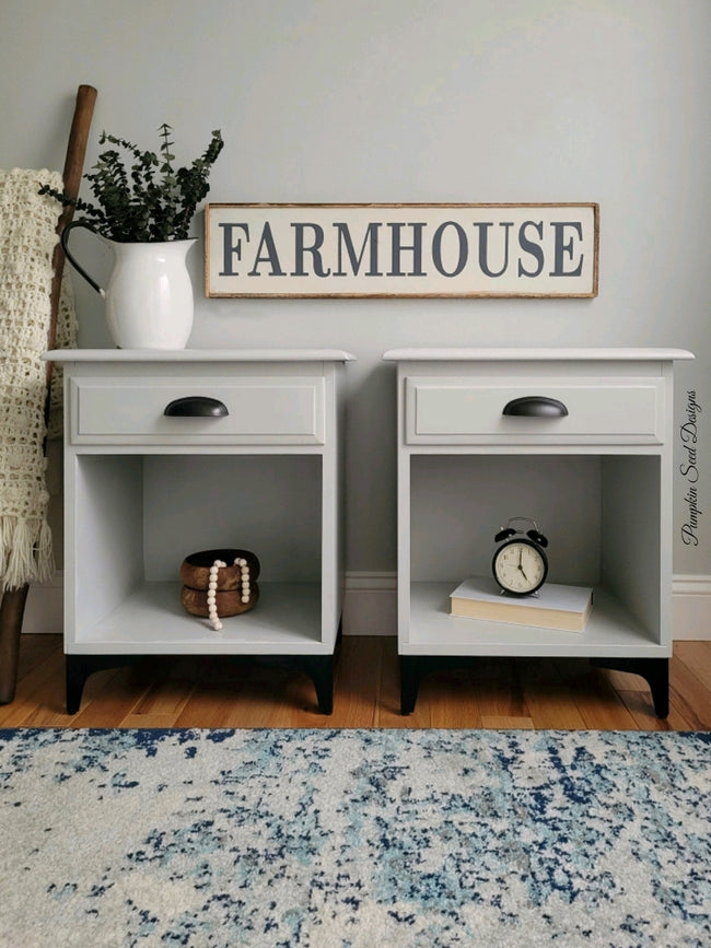 Light grey matching nightstands with black cup pulls black legs and a farmhouse sign