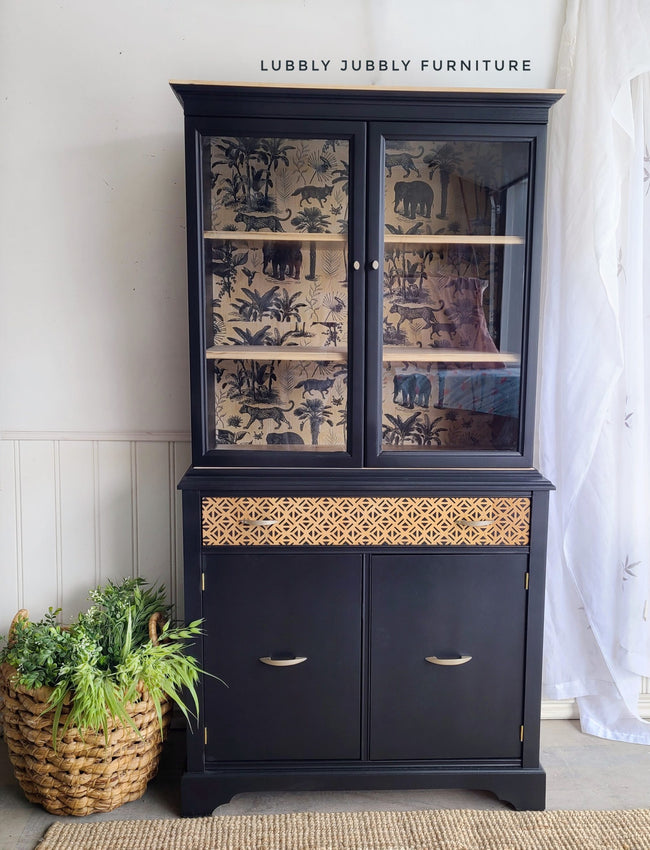 Black painted china cabinet with geometric triangle pattern stenciling and vintage botanical jungle wallpaper