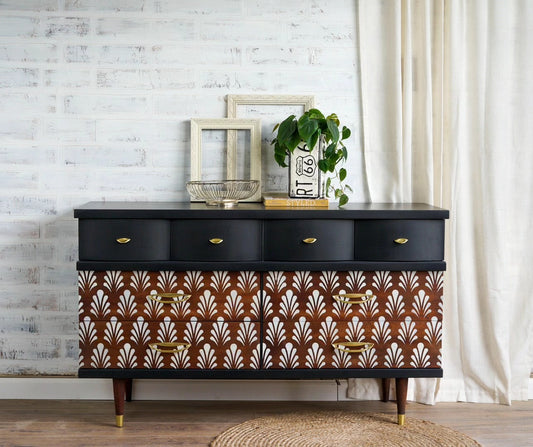 Mid century dresser painted black with stained and stenciled art deco design drawer fronts in front of a white washed brick wall