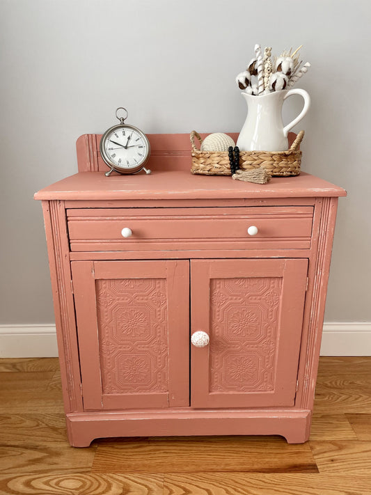 Peach pink painted washstand cabinet with textured wallpaper