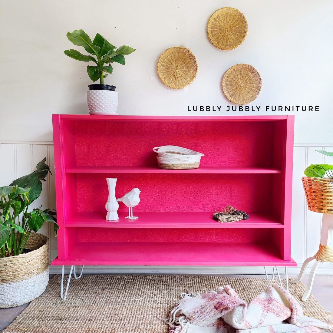 Deep Pink bookshelf on hairpin legs with white geometric design, white pot, ceramic bird, books, potted plants, wicker wall art