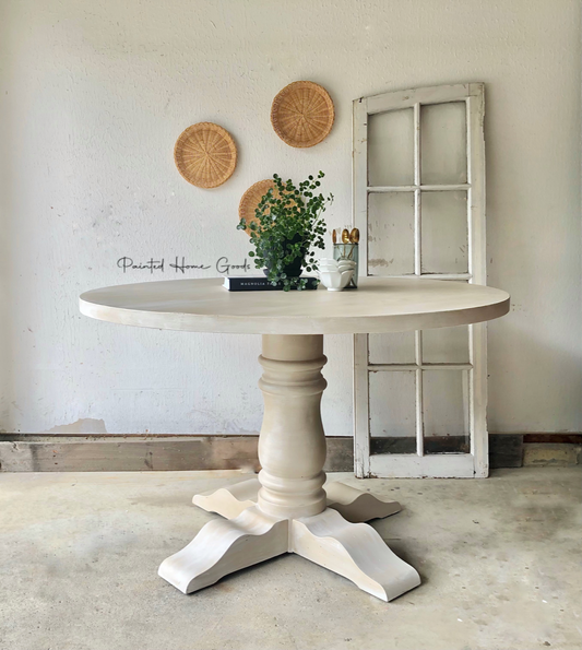 round pedestal dining table in sandy brown, vintage window frame, potted plant, book, wicker wall art