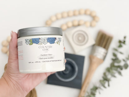 Jar of limestone  furniture glaze in hand with paint brush, eucalyptus, wood bead garland, and sample boards in background