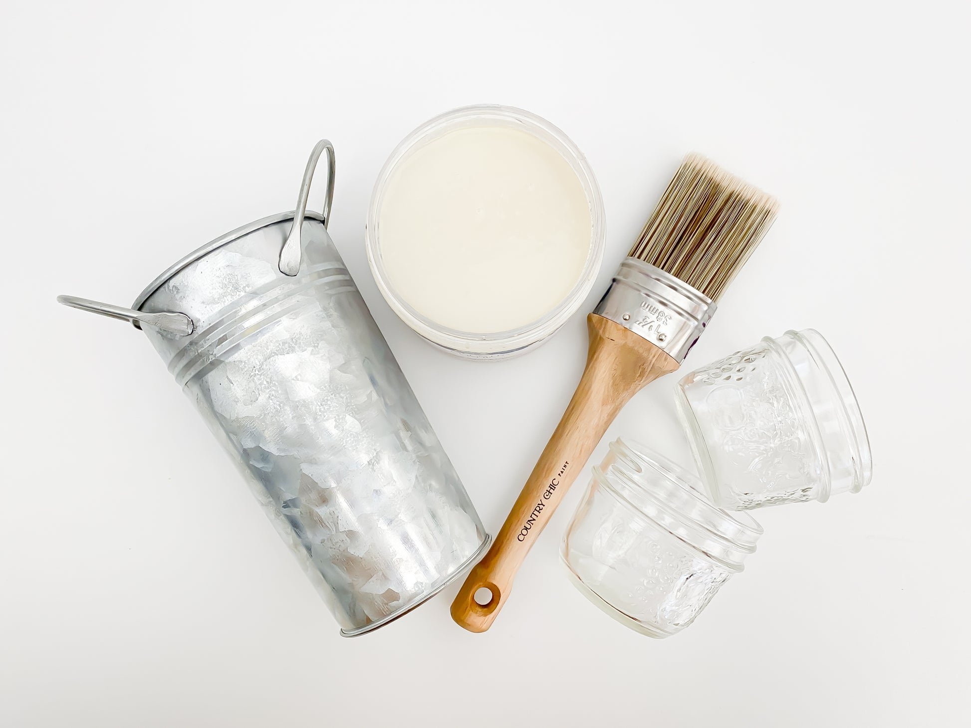 Flatlay of Country Chic Paint Clear Bonding Primer next to furniture paint brush, glass mason jars, and metal can